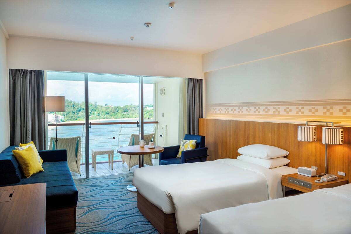 Habitación de hotel con dos camas, un sofá, una mesita y una silla.