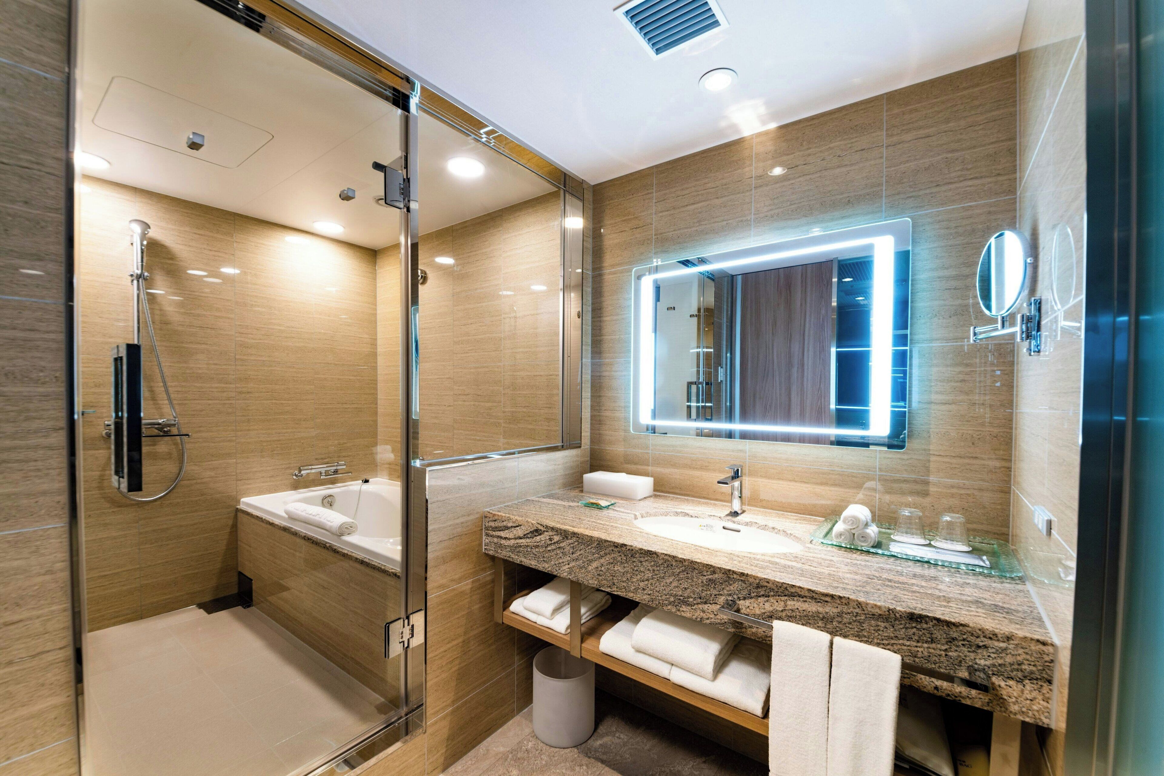A modern bathroom with a glass-enclosed shower, a large mirror, and a granite countertop.