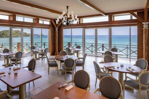 A restaurant with tables and chairs arranged for dining, large windows offering a view of the sea, and a chandelier hanging from the ceiling. - Renaissance Resort Okinawa (Onna)