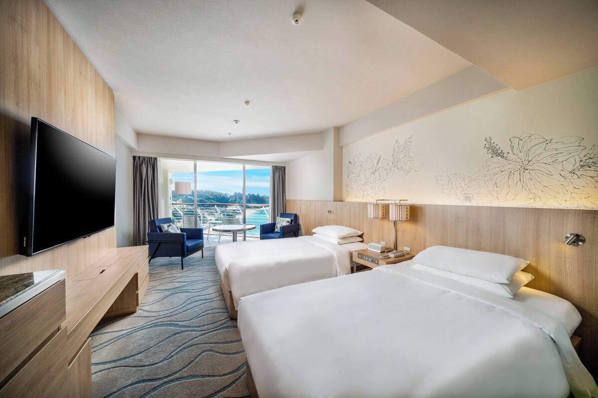 Habitación de hotel con dos camas, televisión, escritorio y vista al océano.