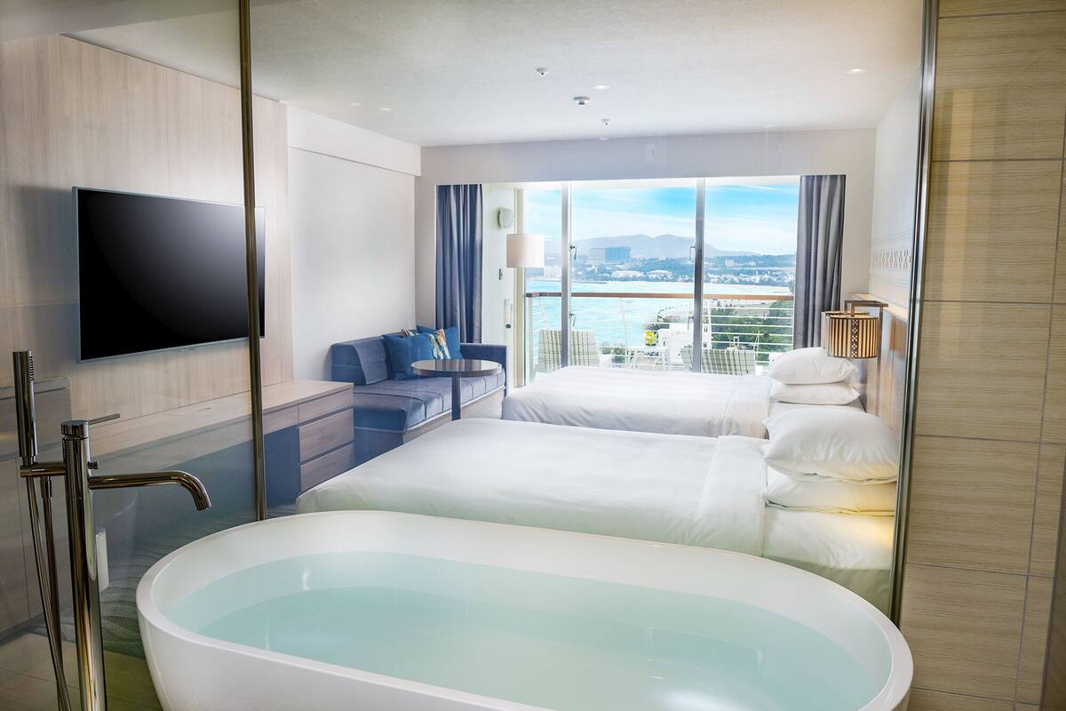 Una habitación de hotel moderna con una bañera grande, un sofá y un televisor.