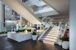 A modern interior with a staircase, seating areas, and potted plants. - Renaissance Resort Okinawa (Onna)