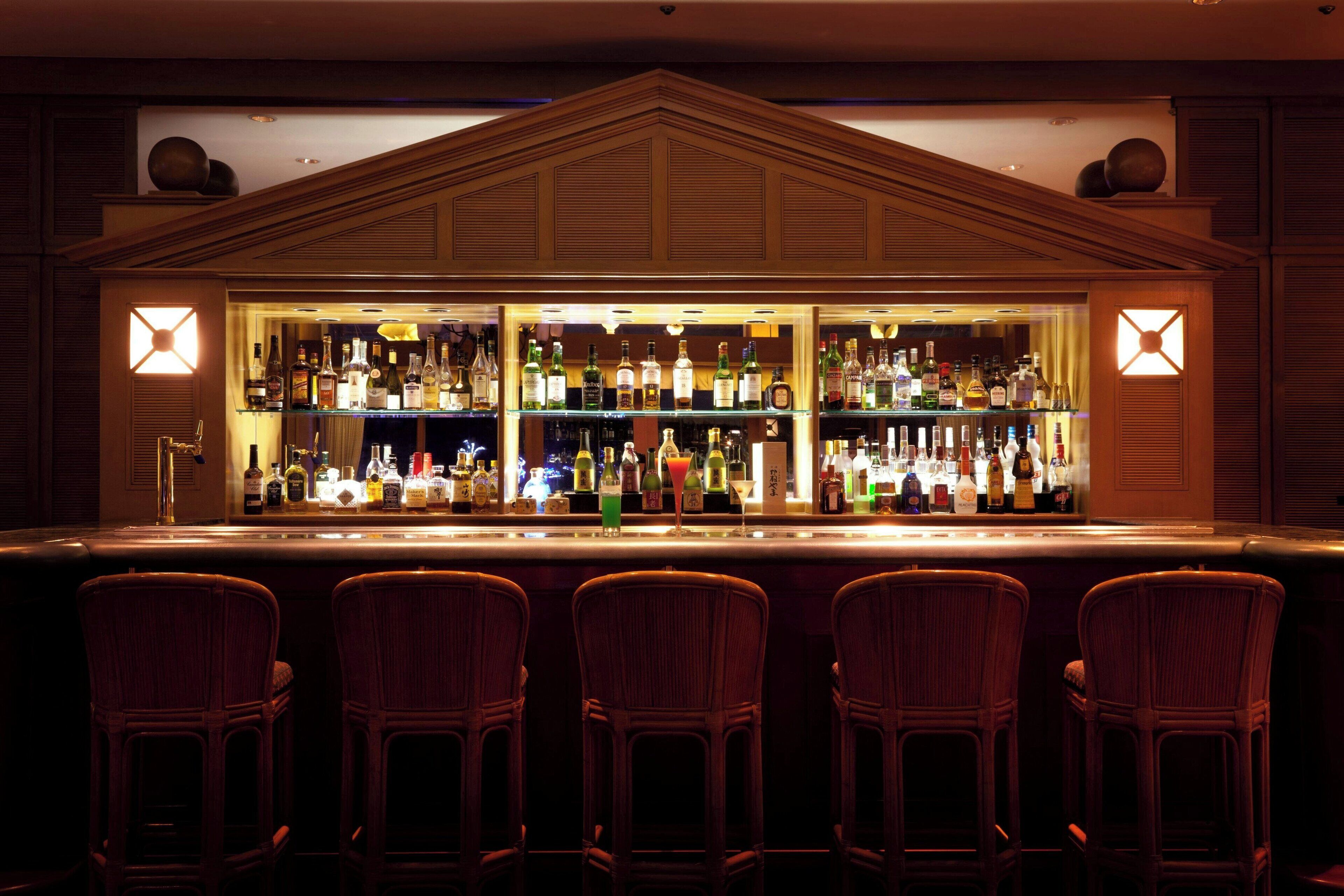 A bar area with multiple liquor bottles, a bar counter, and four wicker bar stools.