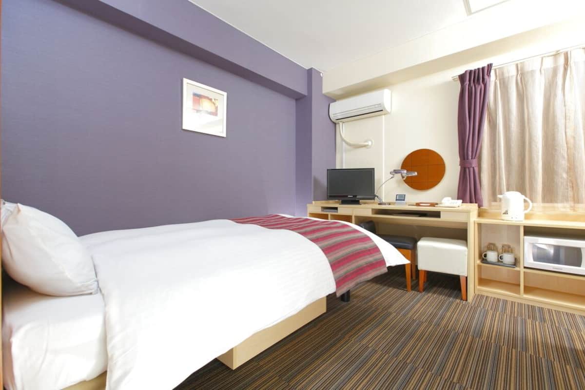Habitación de hotel con cama, escritorio, silla y televisor.