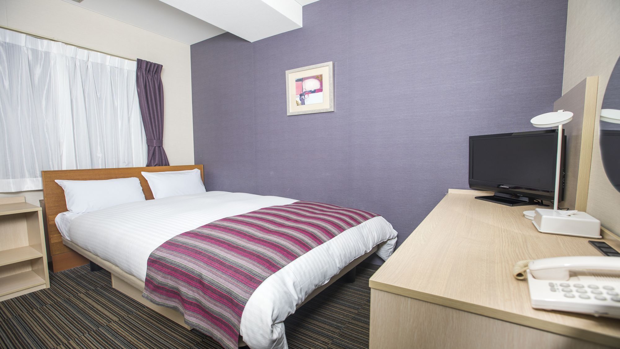 Una habitación de hotel con cama, un escritorio con computadora, teléfono y televisión.