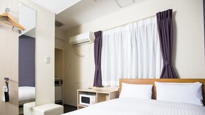 Une chambre d’hôtel équipée d’un lit, d’un bureau, d’une chaise, d’un climatiseur et d’un miroir.