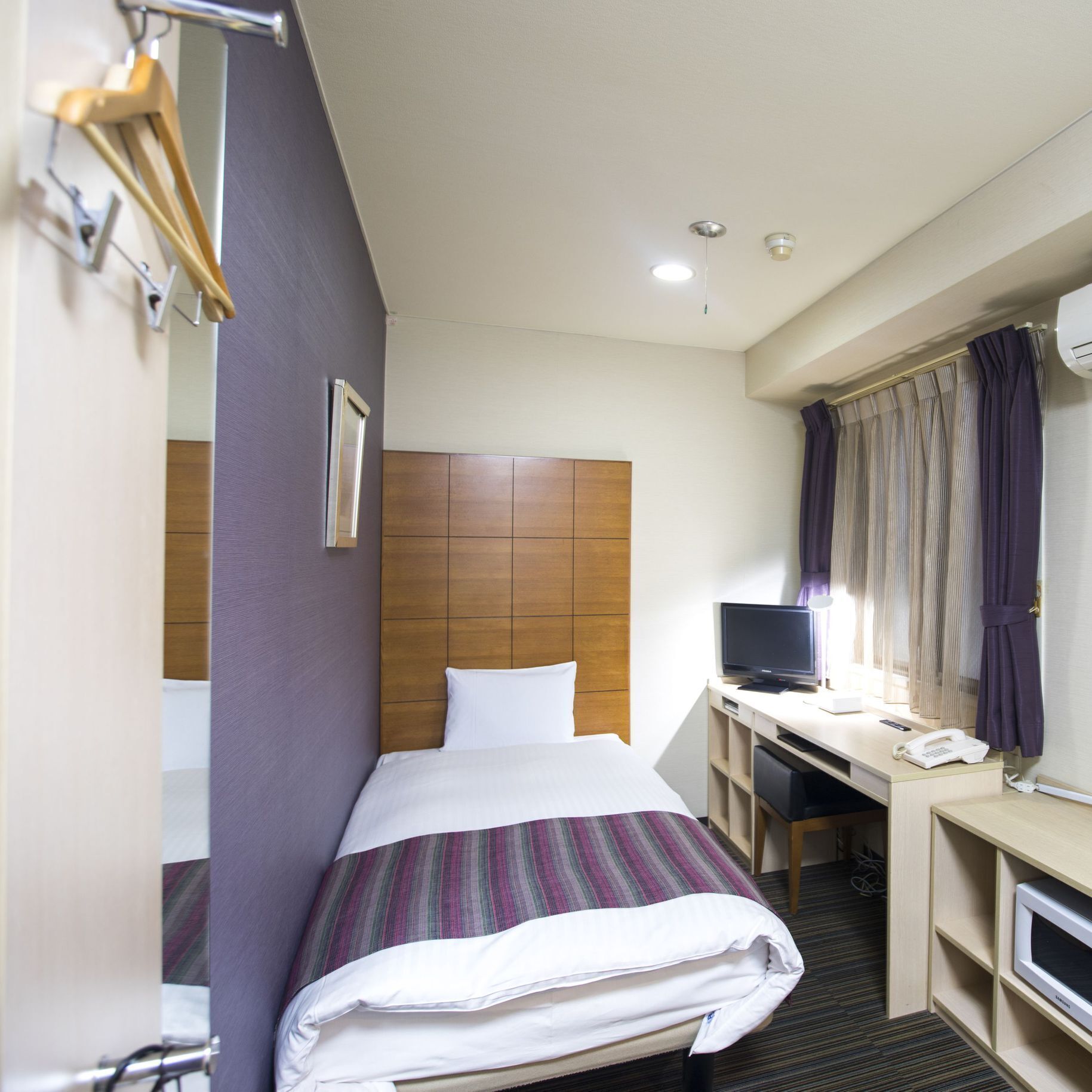 Una habitación de hotel con una cama, un escritorio con computadora, un teléfono y un equipo de aire acondicionado.