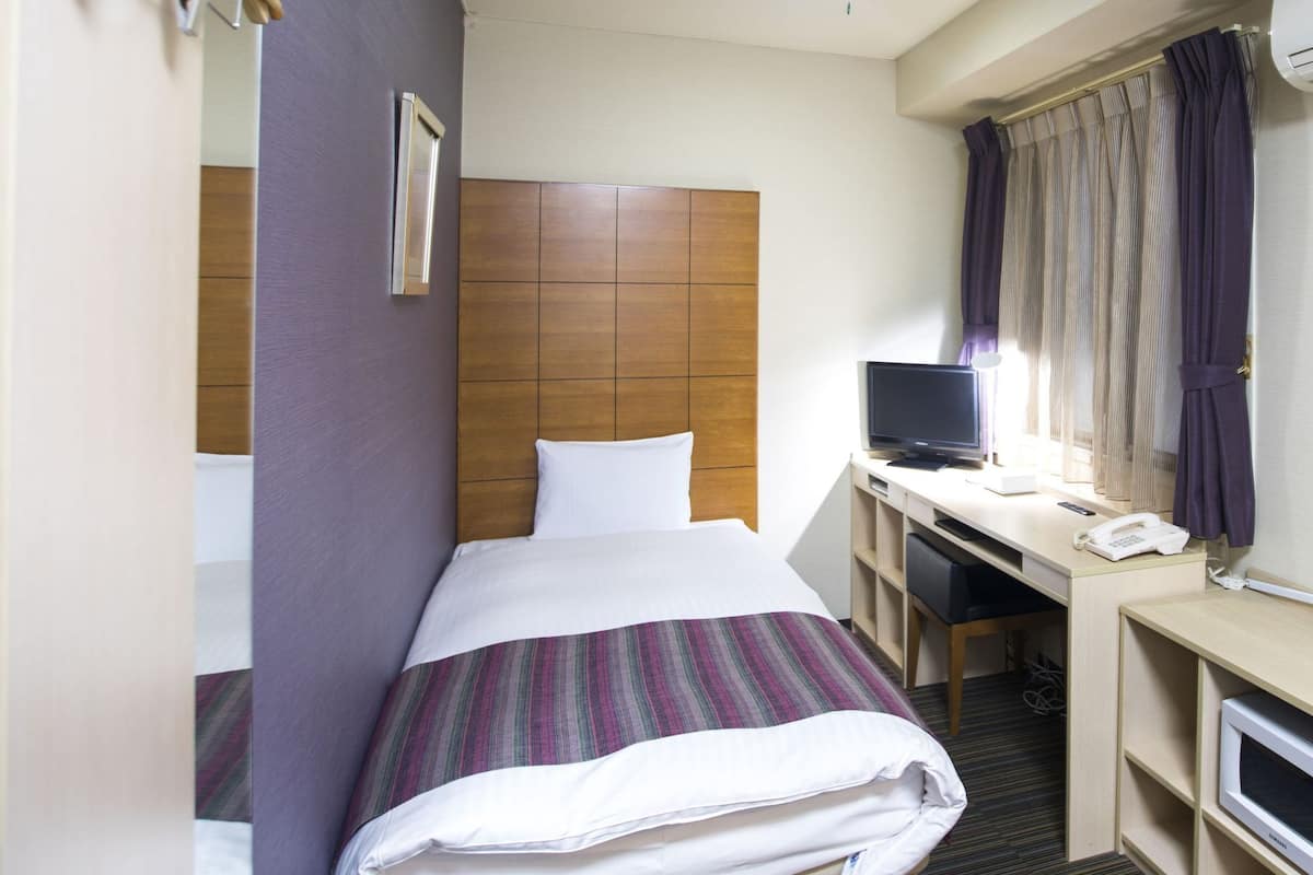 Una habitación de hotel con una cama, un escritorio con computadora, un teléfono y un equipo de aire acondicionado.