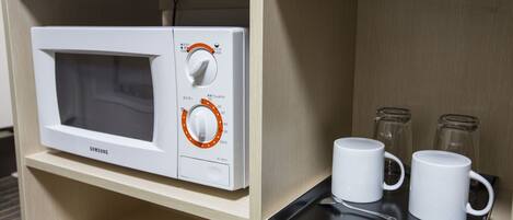 A microwave on a shelf with two white mugs and a spoon on a black tray.