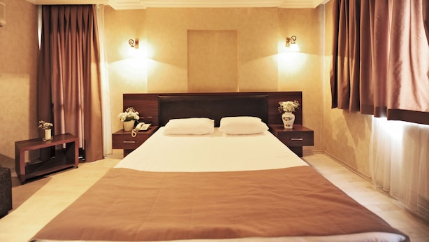 A large bed with a wooden headboard, two bedside tables with lamps, and a nightstand with a vase of flowers. - Üstün Otel Alsancak (Izmir)