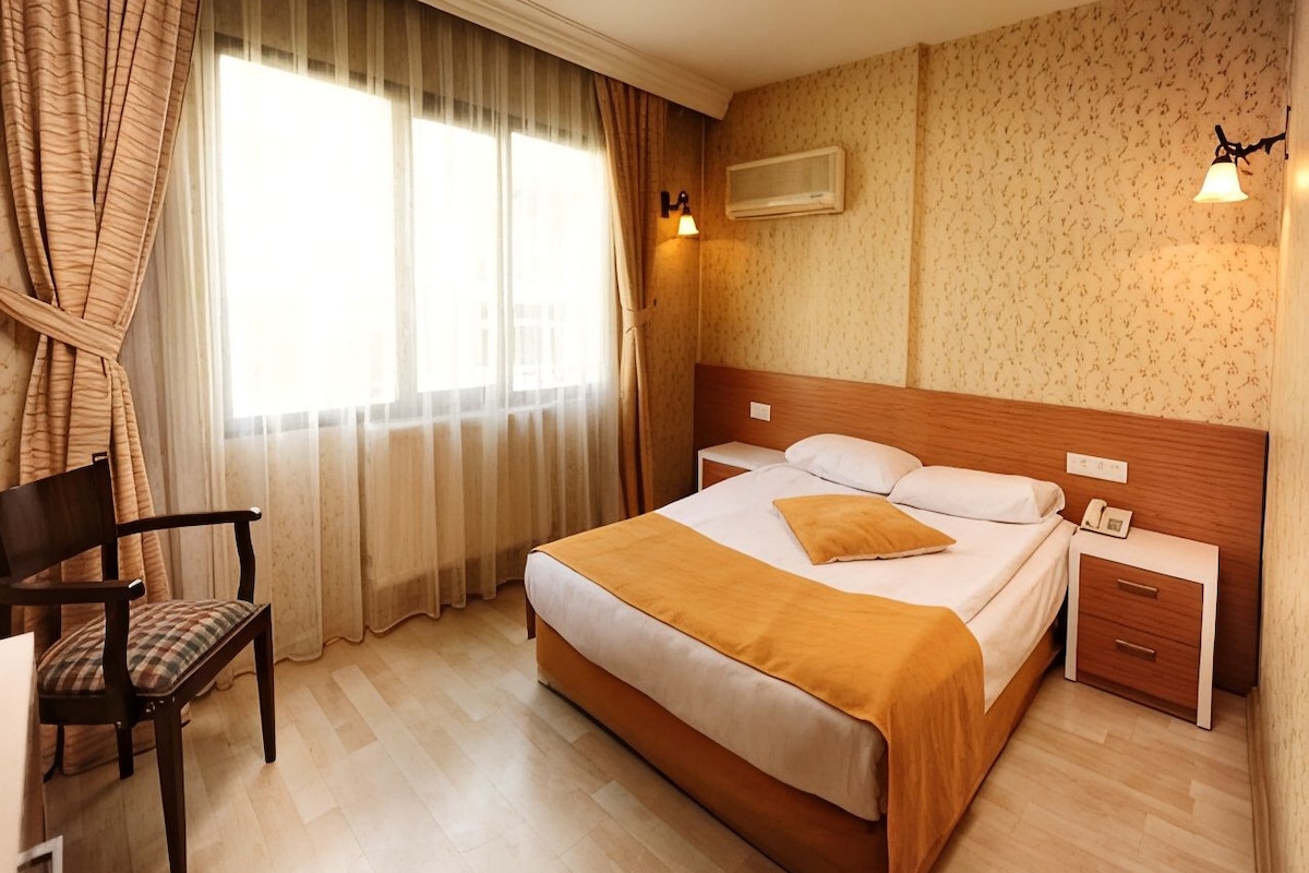 A hotel room with a bed, bedside tables, a chair, and a window with curtains.