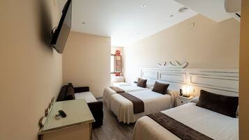 A hotel room with two beds, a desk, a TV mounted on the wall, and a bedside table with a lamp.