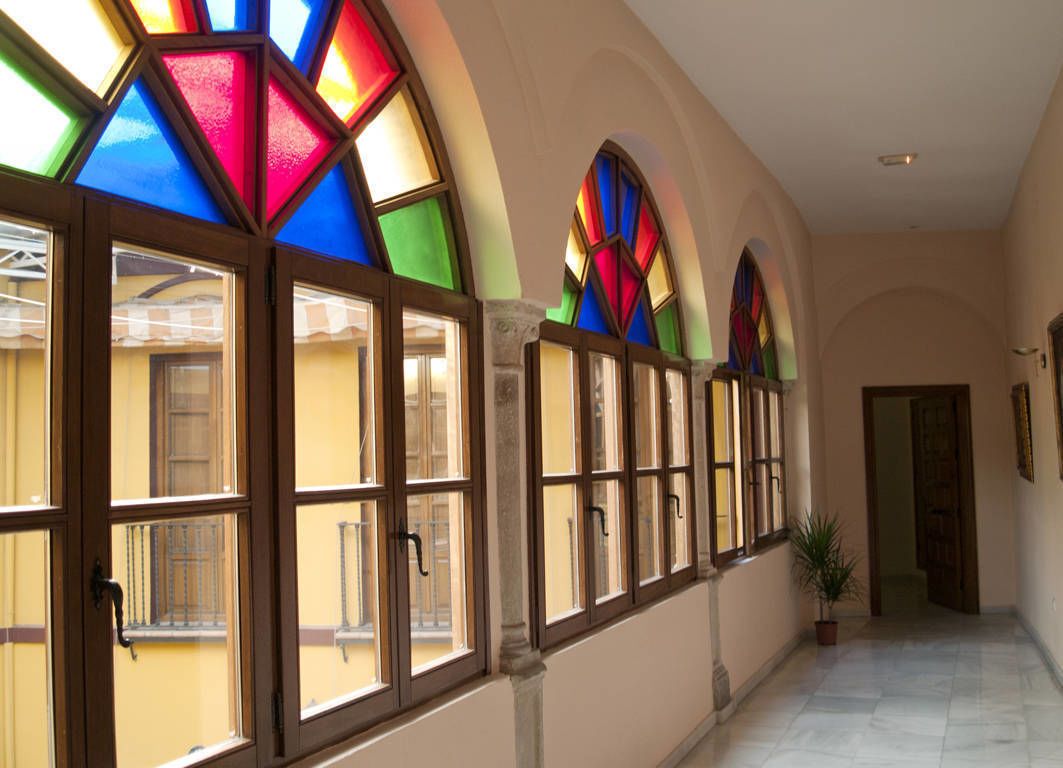 A corridor with large windows featuring stained glass designs, a potted plant, and a door at the end.