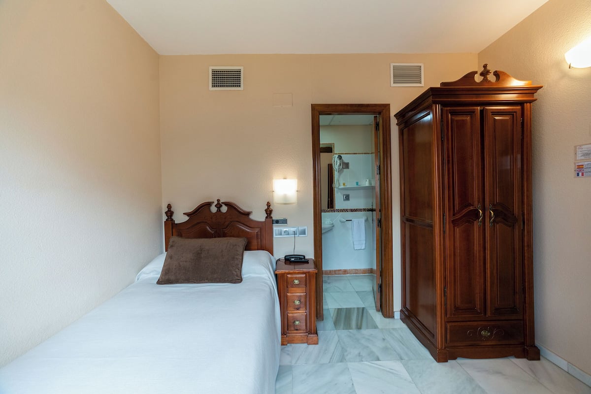 Ein Schlafzimmer mit Bett, einem Holznachttisch, einem Kleiderschrank und einem durchgehenden Türspalt sichtbaren Badezimmer.