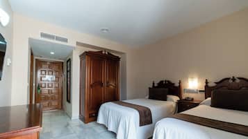 Habitación de hotel con dos camas, un armario de madera, un escritorio y un baño visible a través de una puerta abierta.
