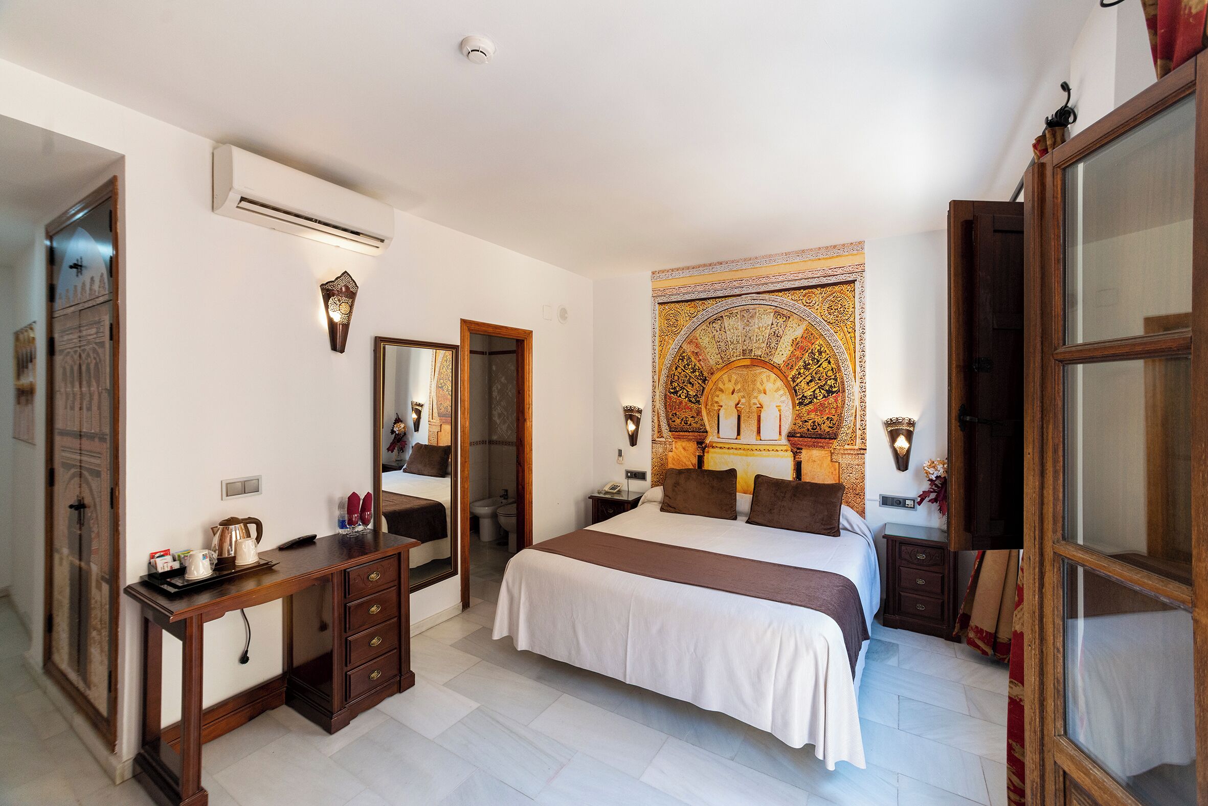 A bedroom with a large bed, a desk, a mirror, and a tapestry.