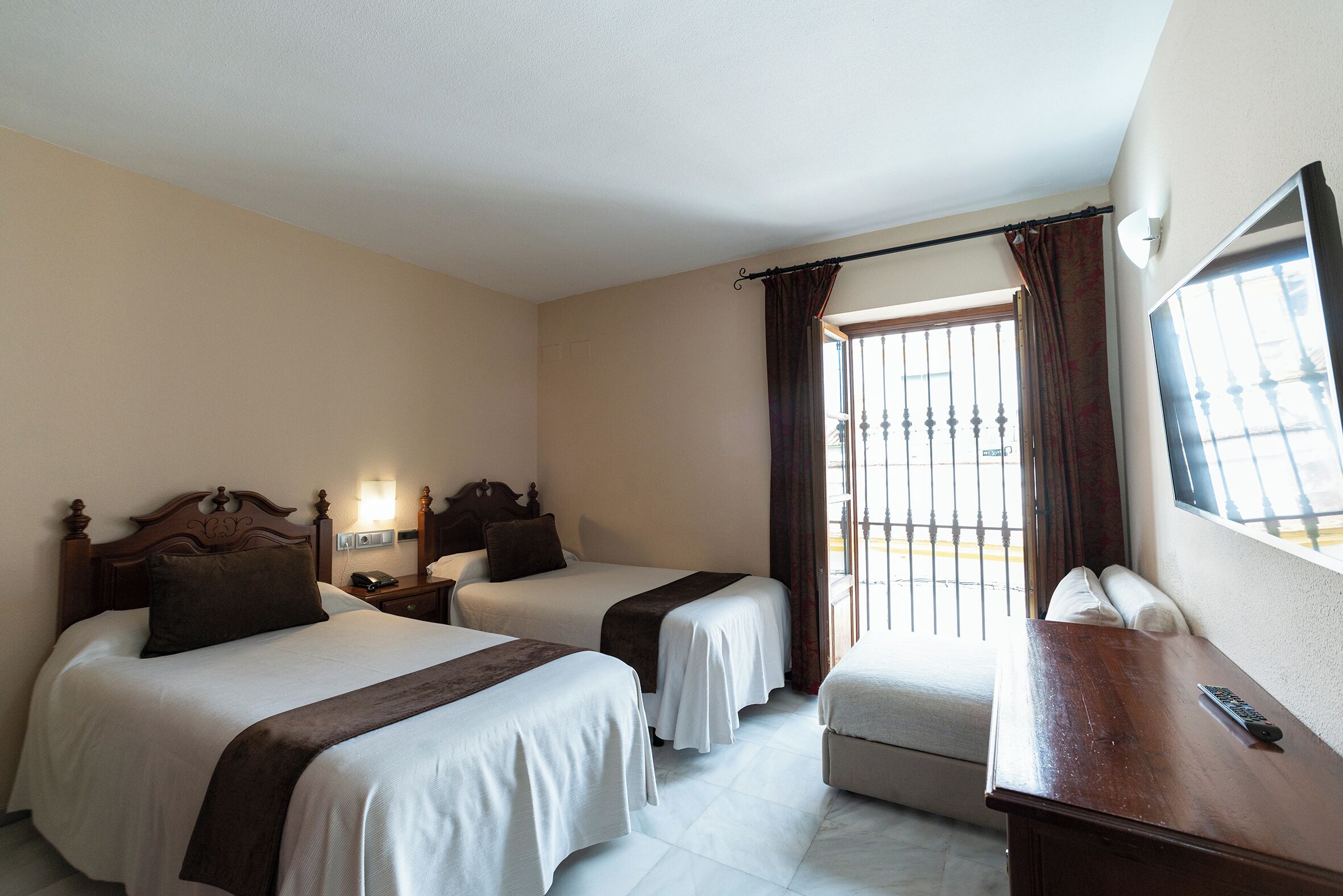 A hotel room with two beds, a desk, a chair, a window with curtains, and a TV.