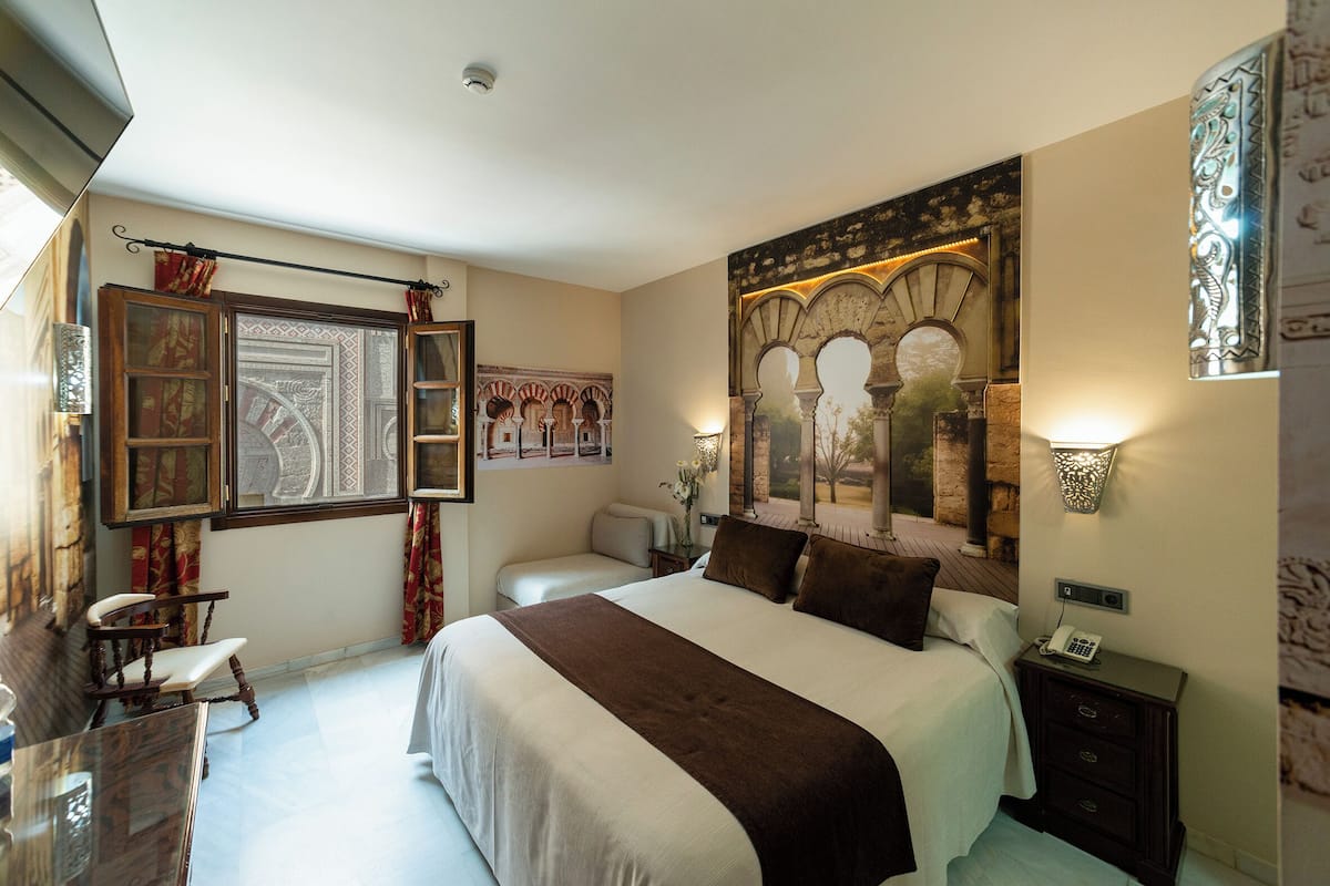 Ein geräumiges Schlafzimmer mit einem großen Bett, einem Schreibtisch und einem Sessel. Eine Zierwand mit Bögen und ein Gemälde sind zu sehen.