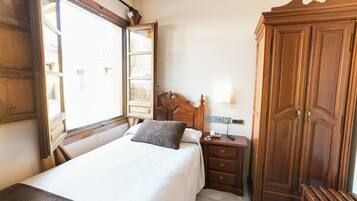 A hotel room with a bed, a wooden wardrobe, a bedside table with a lamp, and a window with curtains.