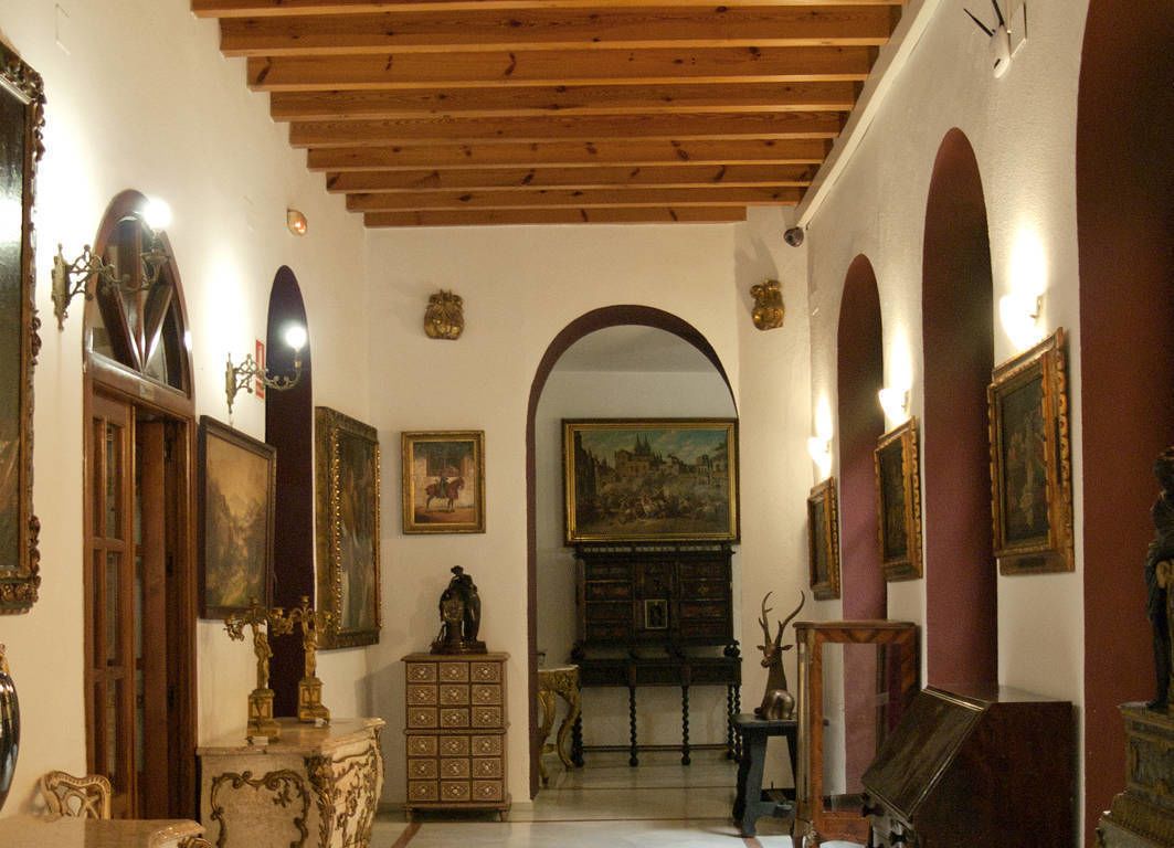 Een kamer met houten balken in het plafond, een grote gewelfde deuropening en verschillende meubelstukken en kunstwerken.