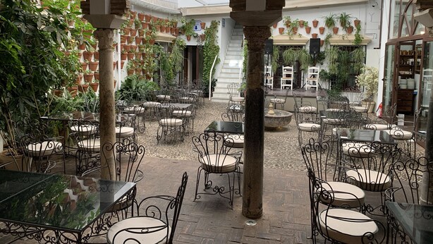 Un patio con mobiliario exterior, plantas en macetas y una escalera que sube a los pisos superiores.