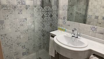 A bathroom with patterned tiles, a glass shower enclosure, a sink with toiletries, and a mirror.