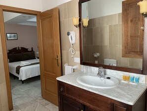 A hotel room with a wooden door, a bed with white linens, a bathroom with a sink, mirror, and toiletries. - Hotel la Chiquita (Córdoba)
