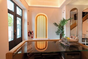 A reception area with a glass desk, a fire extinguisher, a plant, and a mirror reflecting the interior. - Hotel la Chiquita (Córdoba)