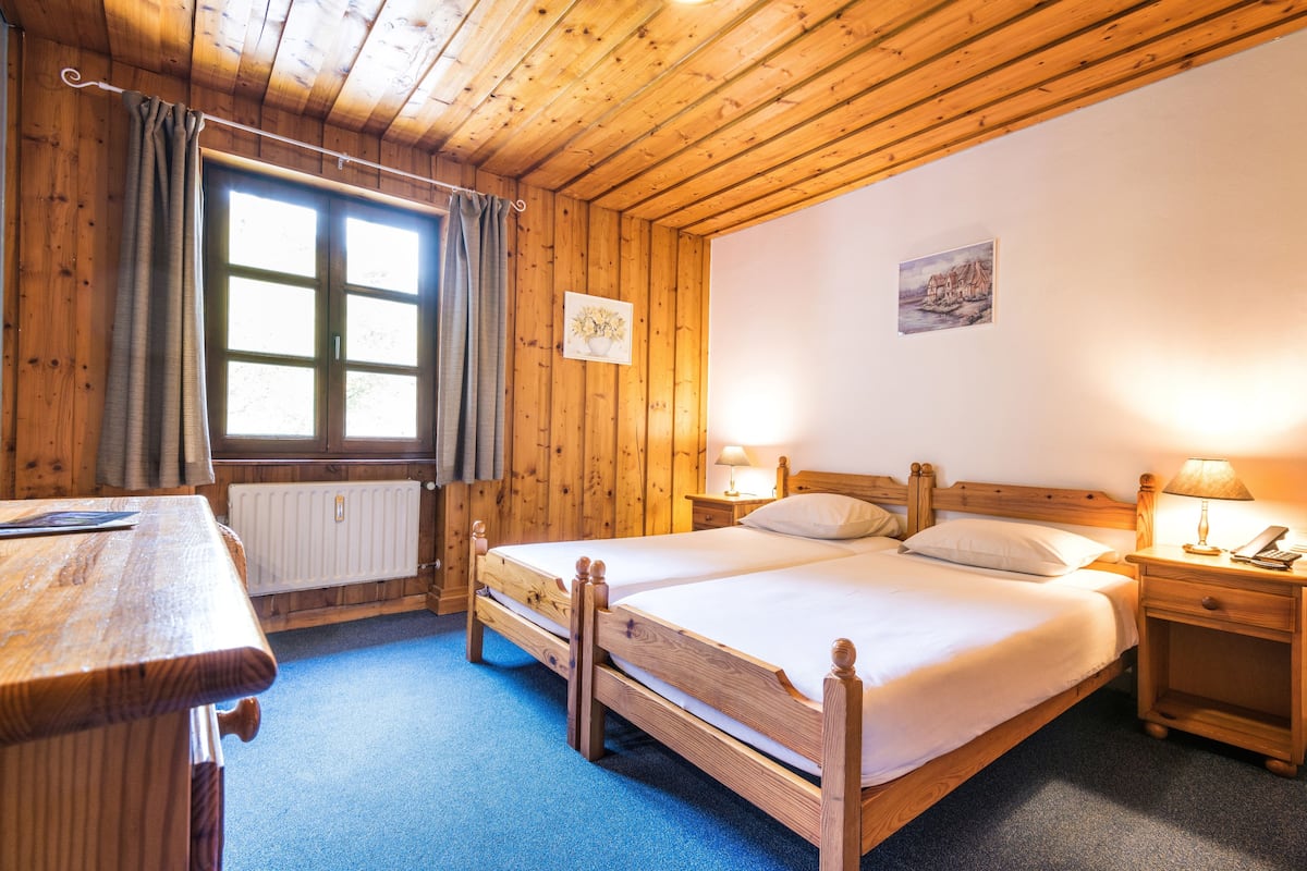 Ein Zimmer mit Holzboden, einem Bett, einem Tisch und einem Fenster mit Vorhängen.