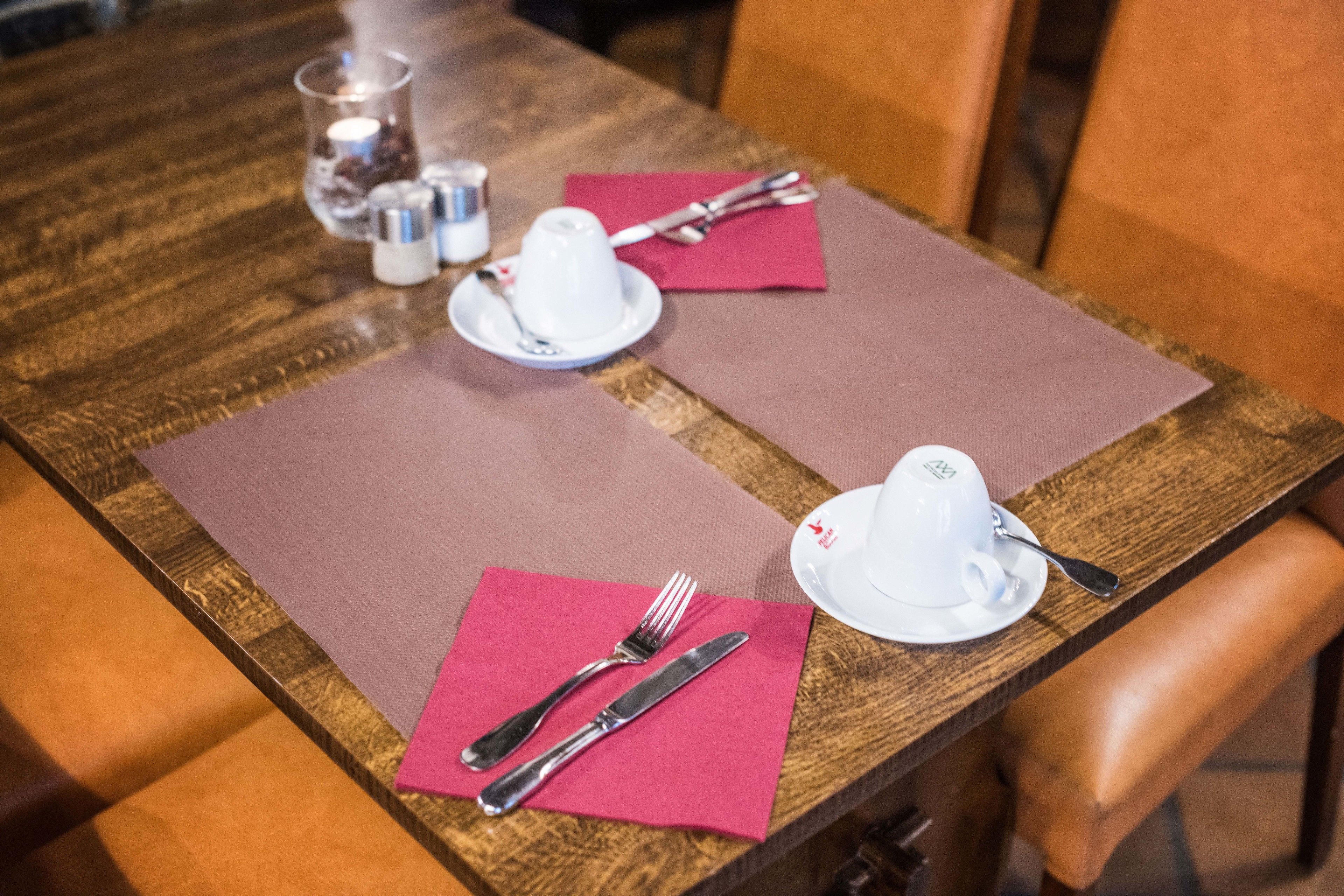 A wooden dining table with four sets of cutlery and plates, each set on a pink placemat.