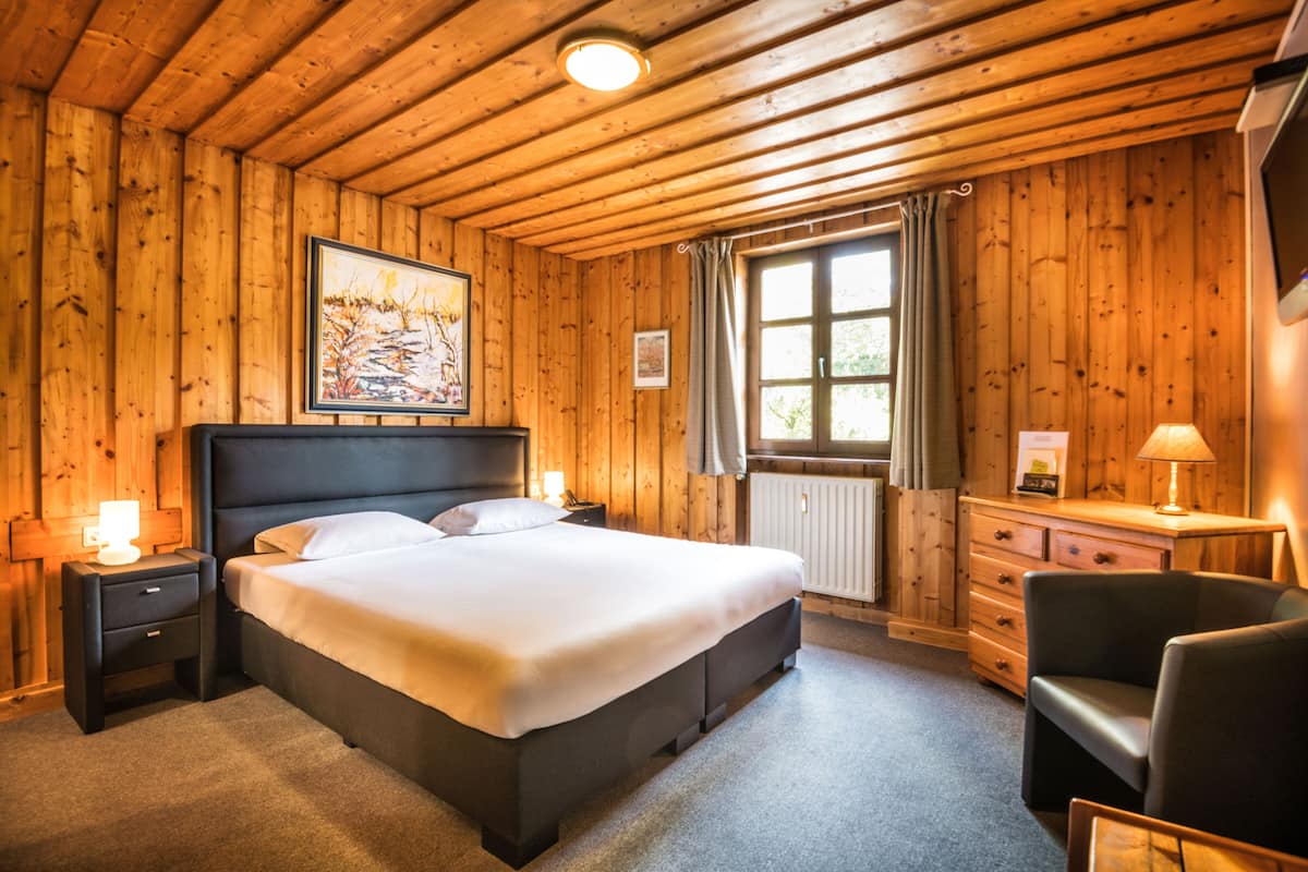 Ein Schlafzimmer mit Holzwänden, einem Bett, Nachttischen, einer Kommode und einem Sessel.
