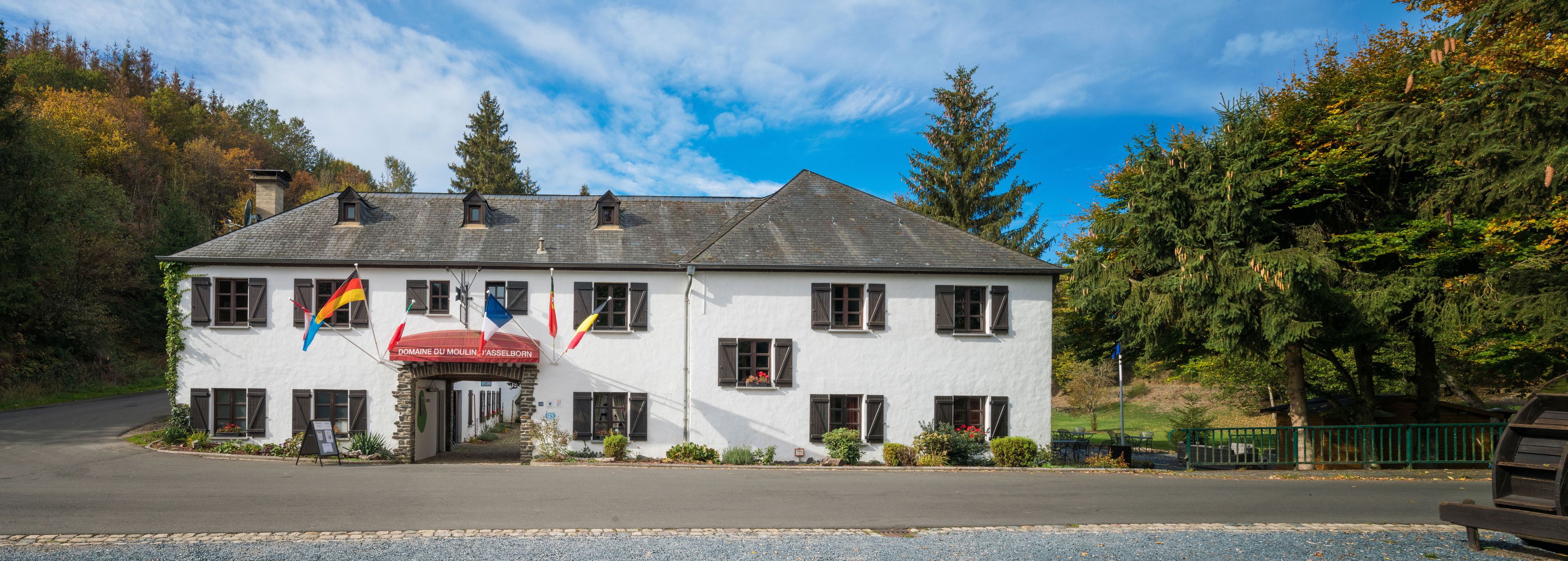 A white building with a steep roof, multiple windows, and a sign reading "Domaine du Moulin".