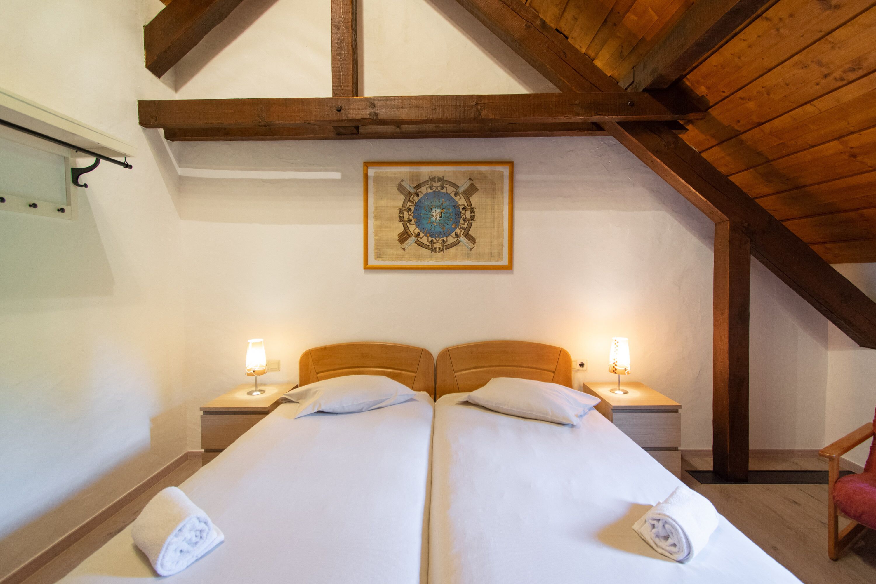 A double bed with two bedside tables, a framed picture on the wall, and a wooden ceiling beam.