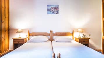 Uma cama de casal com cabeceira e peseira de madeira, duas mesas de cabeceira com abajures e um pequeno quadro na parede.