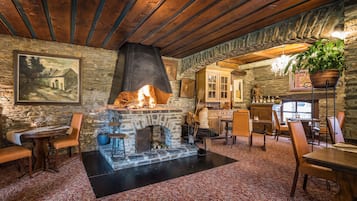 A rustic interior with a stone fireplace, wooden beams, and a dining area with chairs and a table set for a meal.