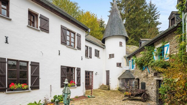 A courtyard with cobblestone paths, white buildings with brown shutters, and a stone tower. - Domaine du Moulin d'Asselborn (Wincrange)