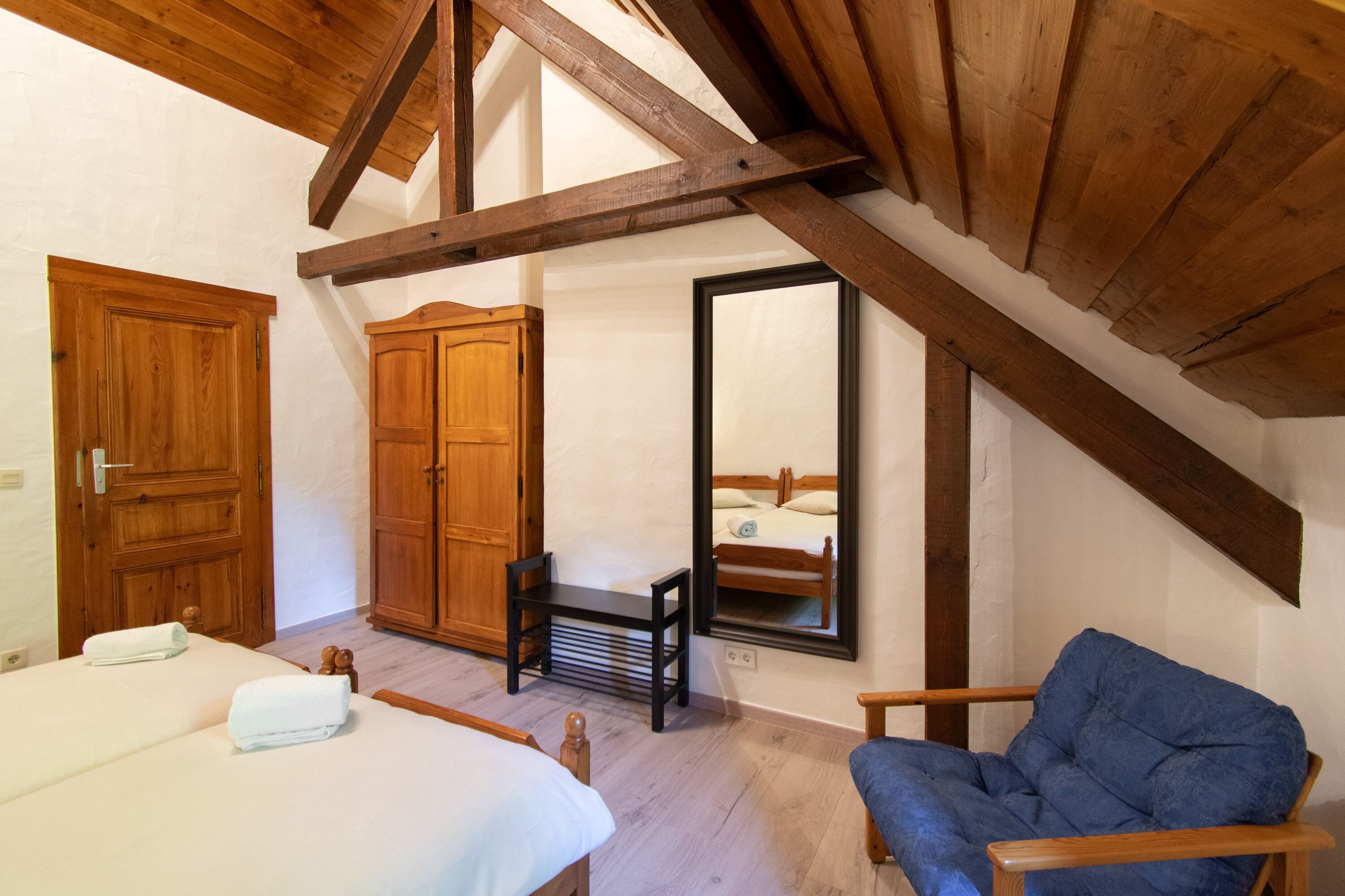 A bedroom with two beds, wooden furniture, a mirror, and a sloped ceiling.