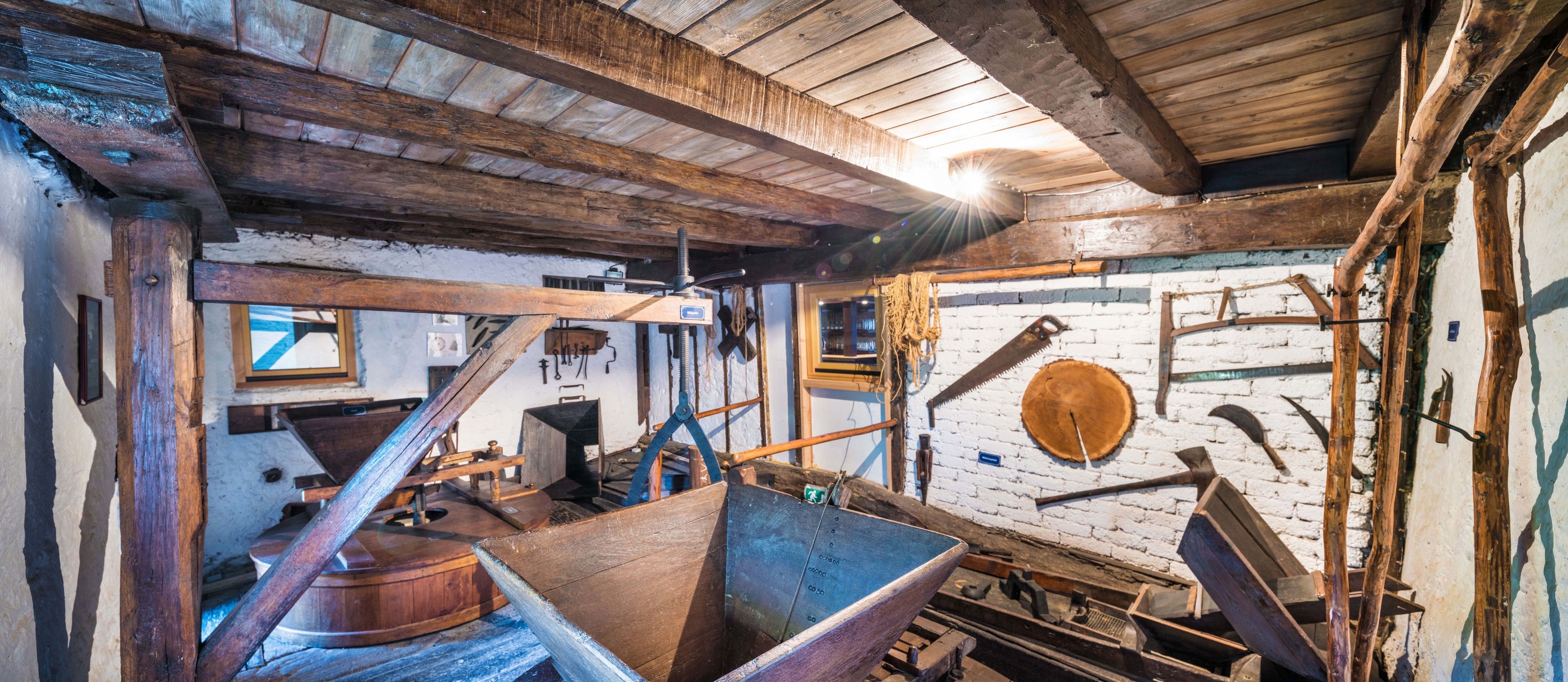 Un interior rústico con vigas de madera, una gran batea de madera y una pared de ladrillo con una rueda de madera.