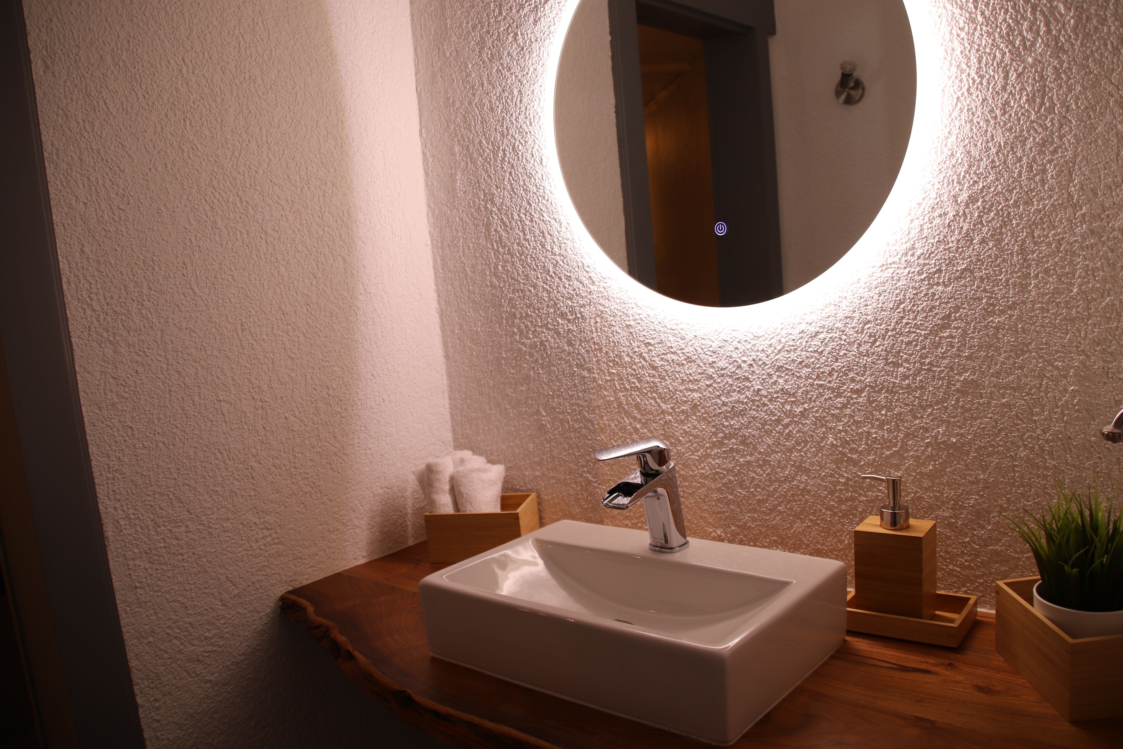 Ein Badezimmer mit einem weißen Waschbecken, einem runden Spiegel und einem Holzkosmetikschrank.