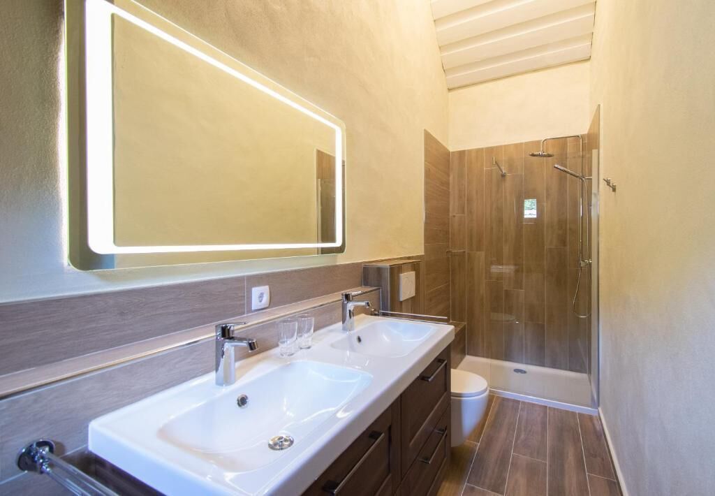 A modern bathroom with a large mirror, two sinks, and a shower.