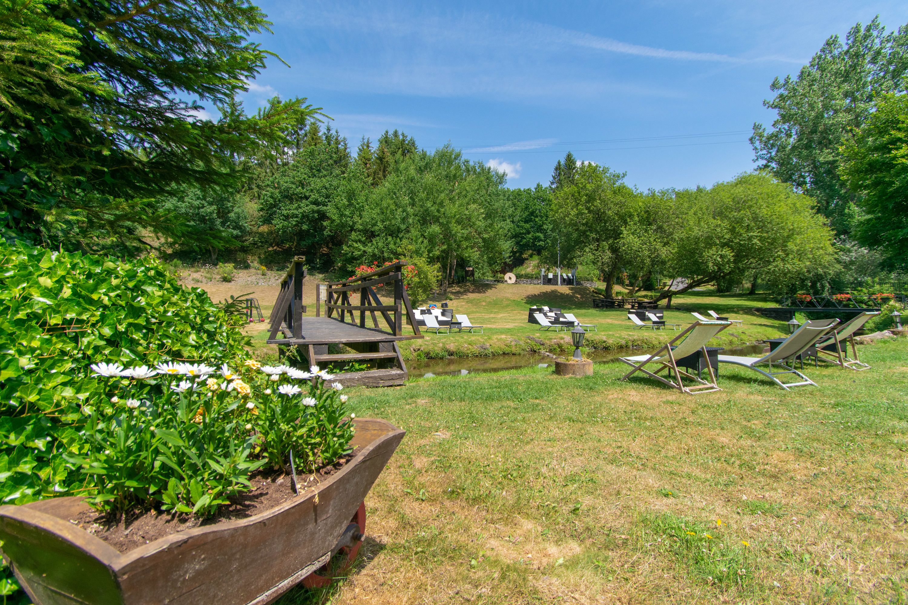 Un jardin avec une terrasse en bois, des chaises longues et un parterre de fleurs.