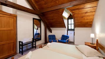 Un dormitorio con una cama grande, dos sillas azules, un armario de madera, un espejo y una mesita de noche con una lámpara.