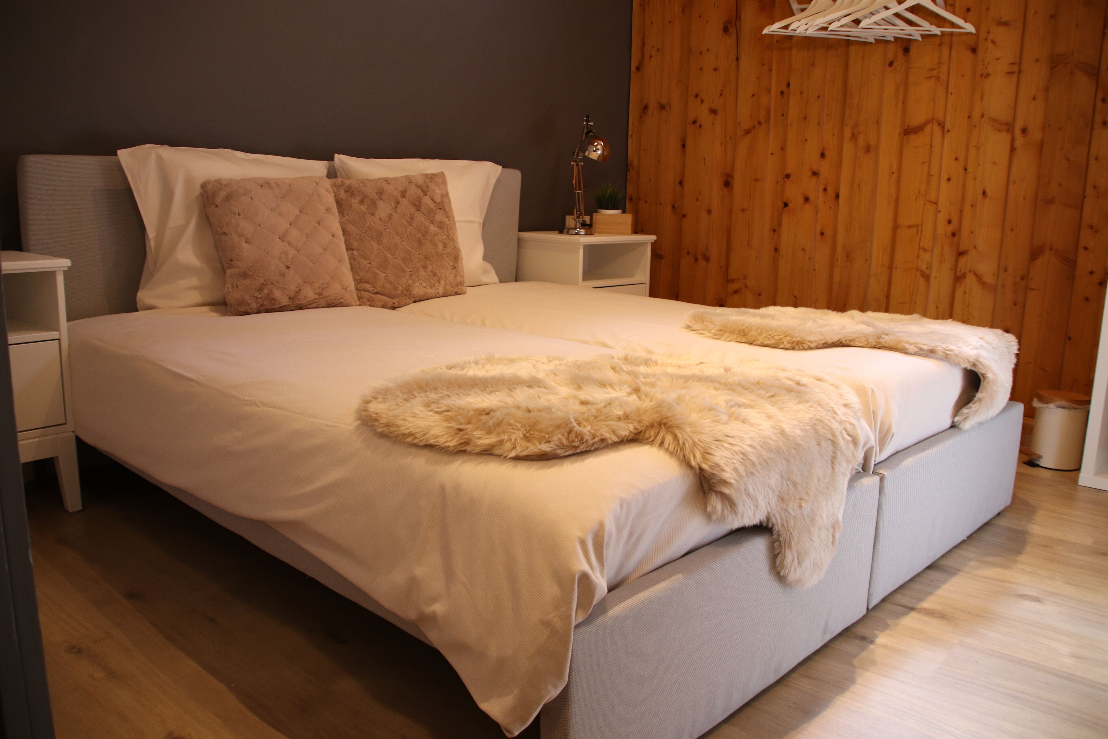 Une chambre avec un grand lit, deux tables de chevet, une lampe et un mur en bois.