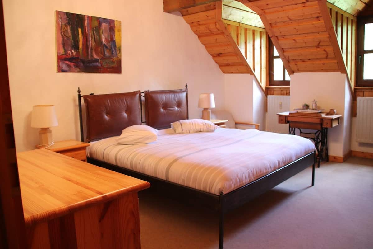 Ein Schlafzimmer mit einem Bett, zwei Nachttischen, einem Schreibtisch und einem Gemälde an der Wand.