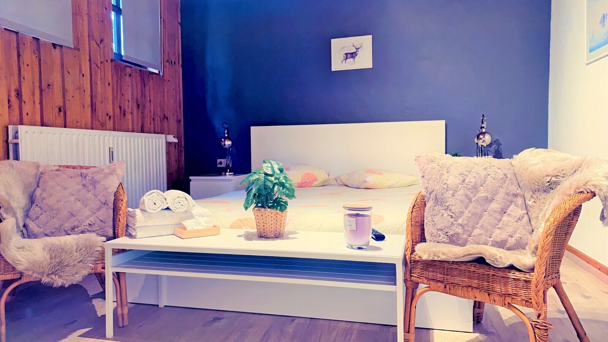 Une chambre à coucher comprenant un lit, deux chaises, une table de chevet, un radiateur, une lampe fixée au mur et un tableau encadré.
