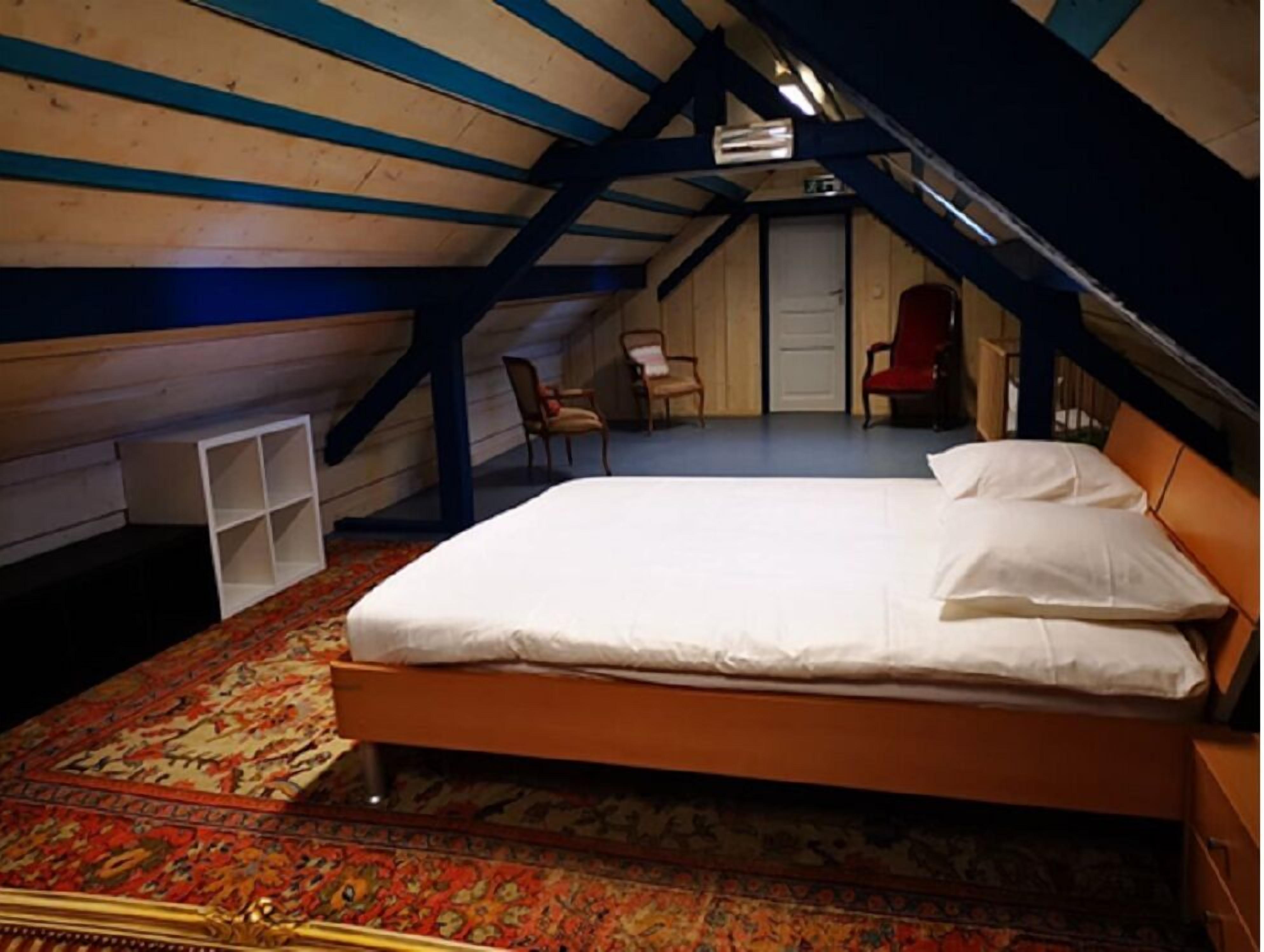 Een slaapkamer met een bed, een stoel, een klein wit rekje en een deur.