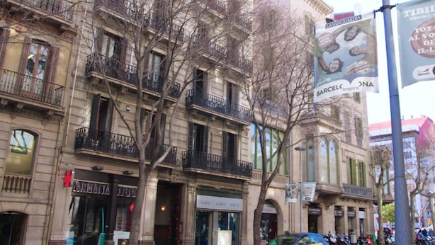 A multi-story building with balconies, storefronts, and a parked car. - Lenin Hostel Barcelona (Barcelona)