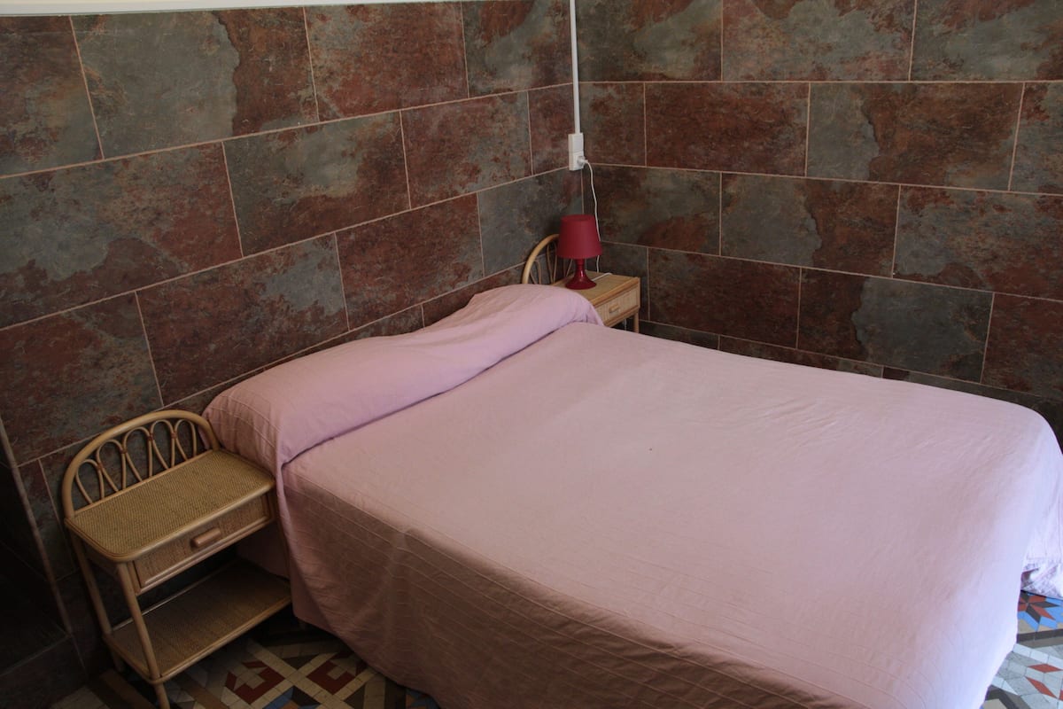 A bedroom with a bed, a nightstand, a lamp, and a chair.