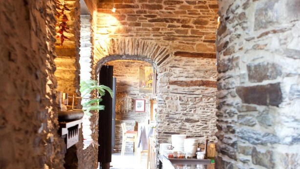 Ein Korridor mit Steinwänden und Holzboden, der zu einer Bar mit Theke und Hockern führt.