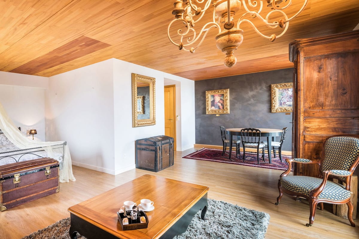 A cozy room with a bed, a wooden coffee table, a chair, a dining table, and a chandelier.